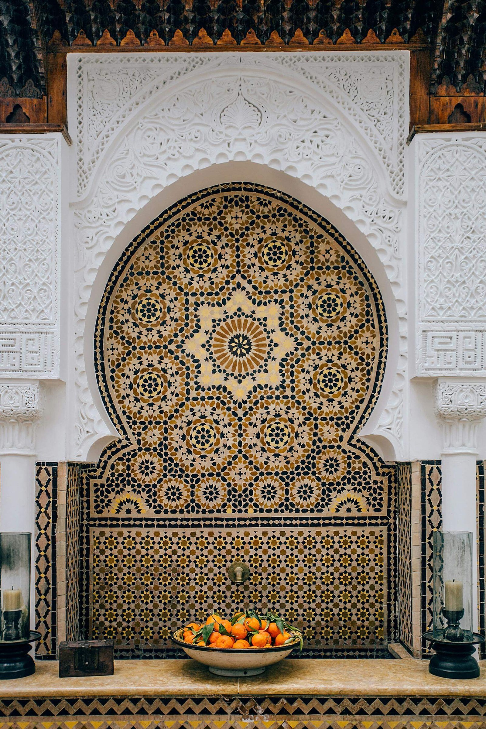 The-image-depicts-a-traditional-Moroccan-riad-courtyard-adorned-with-intricate-zellige-tilework-and-beautifully-carved-plasterwork,-showcasing-the-rich-heritage-and-craftsmanship-of-Moroccan-culture.-Lush-greenery-and-ornamen.jpg