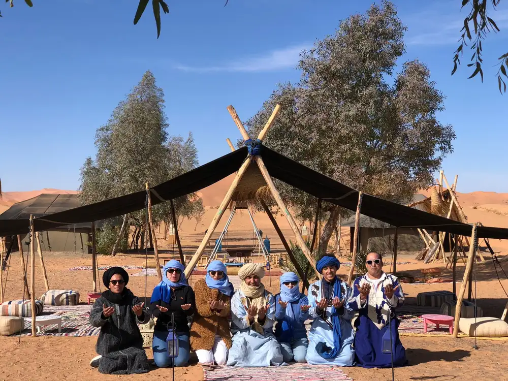 Travelers sitting with the camp team under the tent at the desert camp near Merzouga